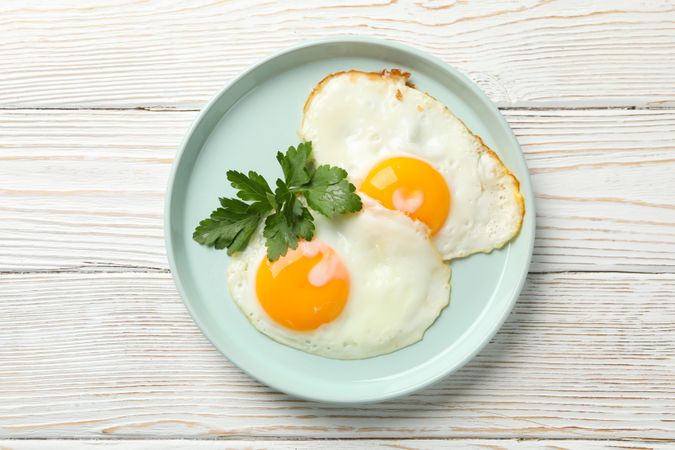 Top view of two eggs sunny side up on blue plate