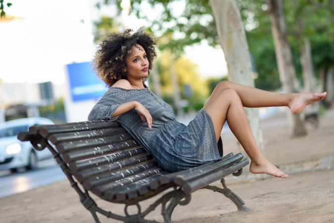 Wistful female in casual dress sitting on park bench and thinking