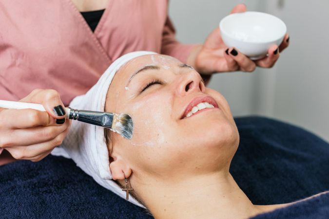Anonymous professional beautician applying facial mask on face of client
