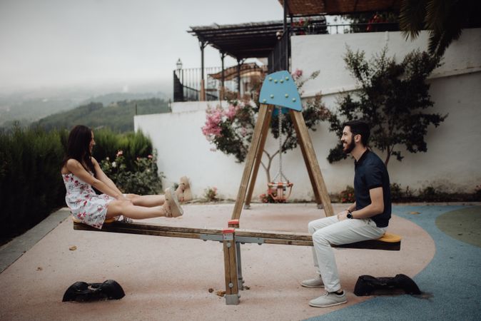 Playful couple swinging on seesaw on playground at rural street