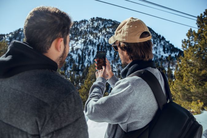 Men with smartphone and camera on hill between trees in winter