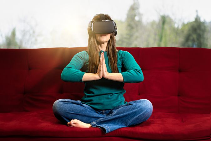 Woman in VR glasses sits in a lotus yoga position with hands together