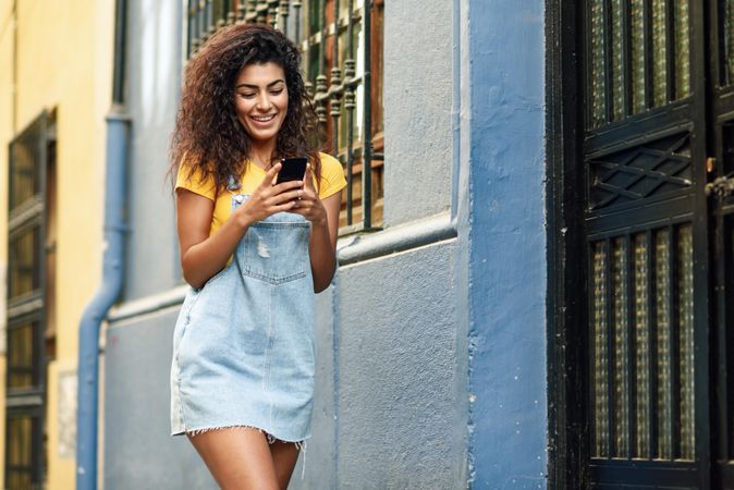 Smiling woman checking phone in front of metal door