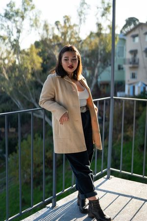 Full length of young woman in stylish wool coat standing on outside patio with view