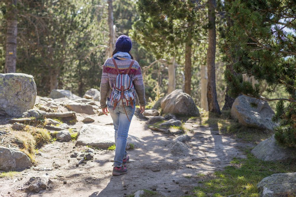 Back of woman walking through rocky forest on sunny day