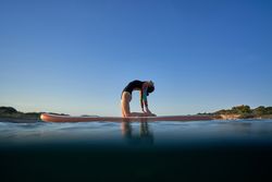 Slim woman practicing yoga in Camel pose on paddleboard in sea