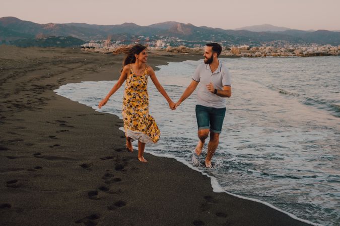 Lovely couple running holding hands on sandy beach