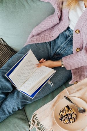 Top view of woman in pink sweater and blue denim jeans reading book