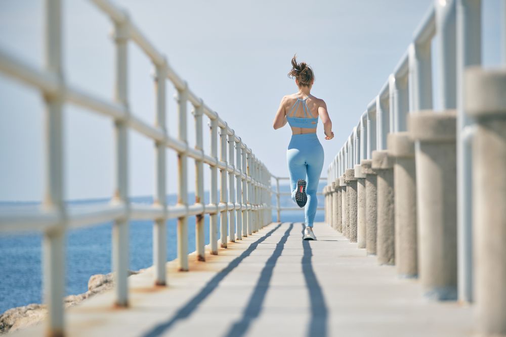 Unrecognizable jogger running on bridge above ocean during worko