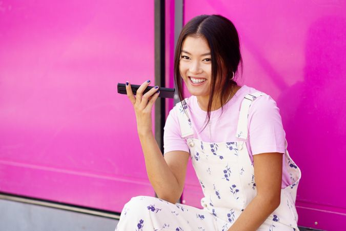 Smiling Chinese woman talking on cell phone sitting next to pink
