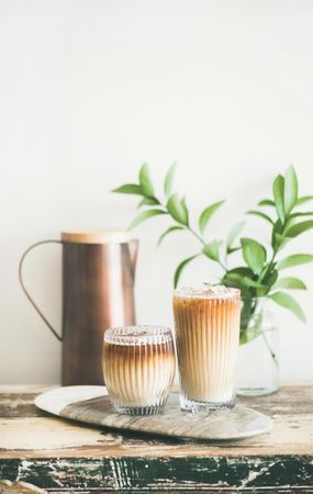 Two glasses of iced coffee glasses and a pitcher, with light background with leaves