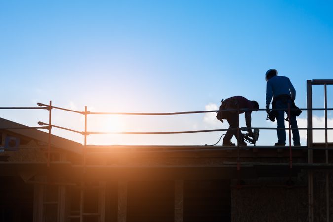Construction Workers Silhouette on Roof of Building