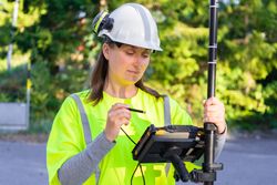 Woman wearing construction helmet and yellow vest working on machine