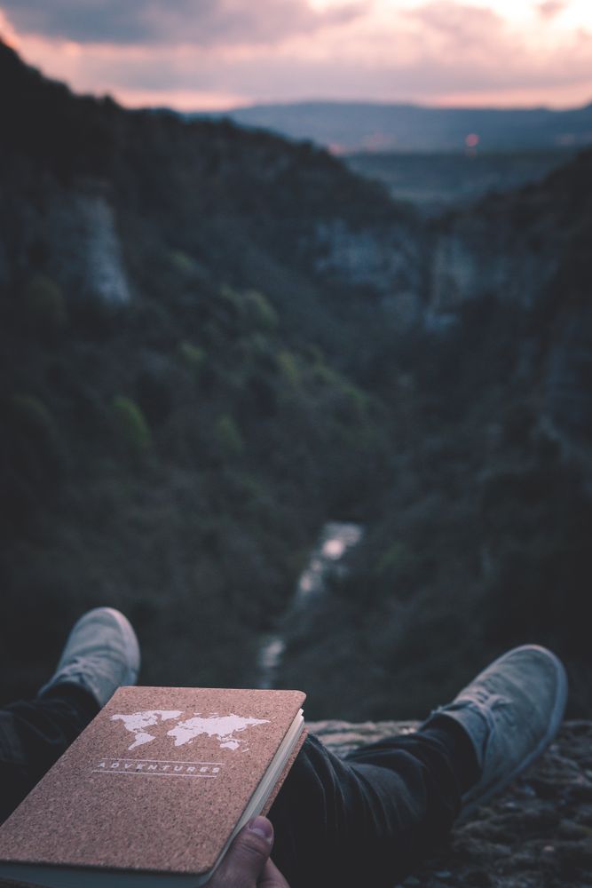 View to small river in canyon and legs of person with book sitting on the edge