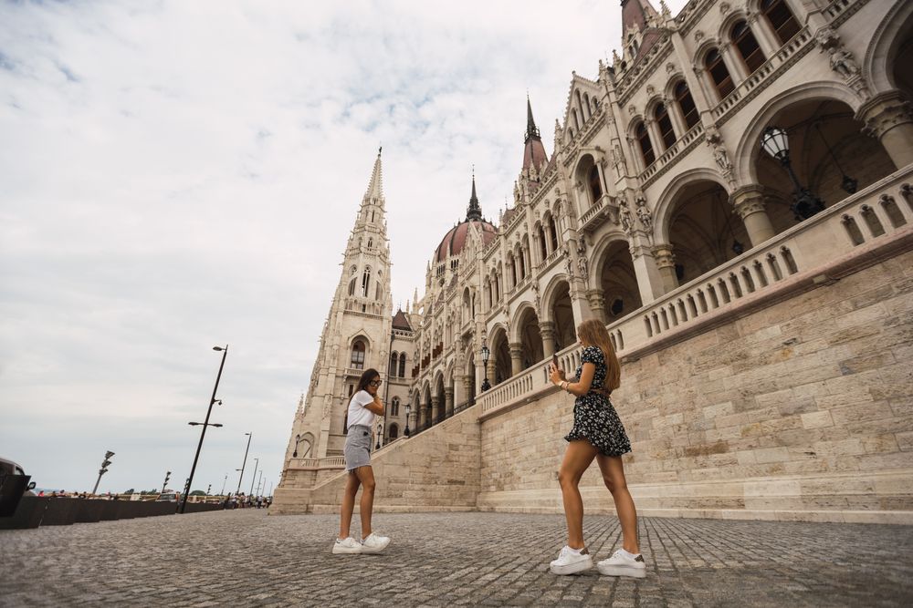 Stylish women taking photos on square against old building