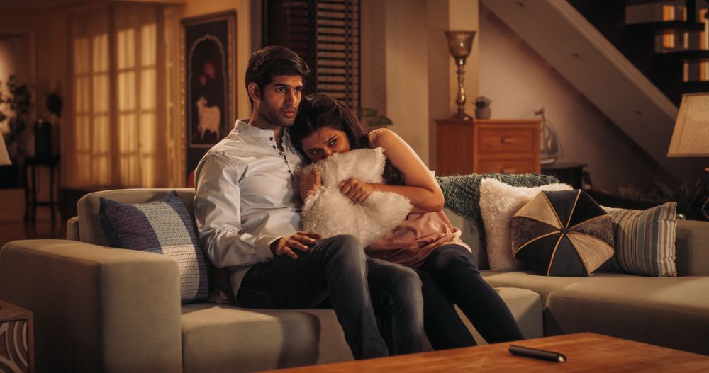 Young Indian Couple Watching Scary Movie on TV, Finds Comfort In Each Other's Arms As They Sit On Their Couch.