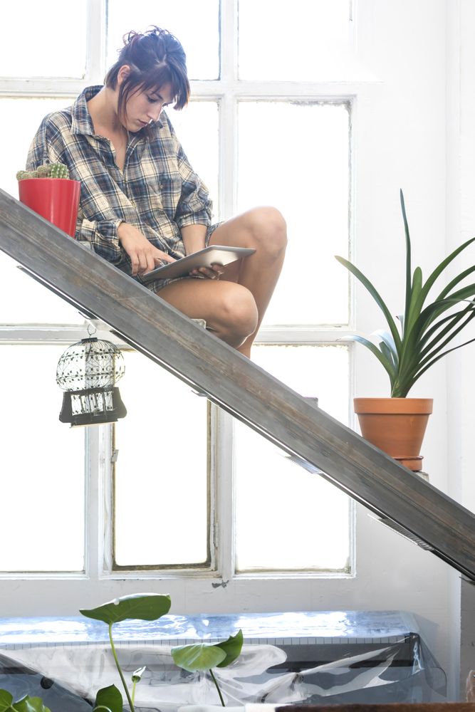 Side view of female in flannel shirt lounging at home with digital tablet, vertical
