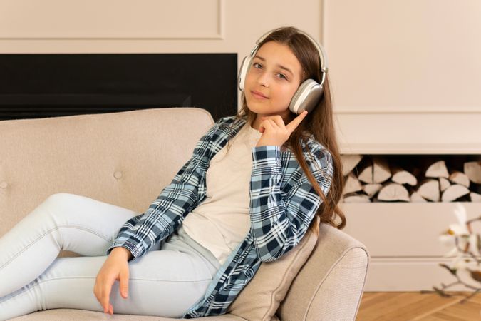 Teen girl relaxing comfortably on sofa listening with headphones.