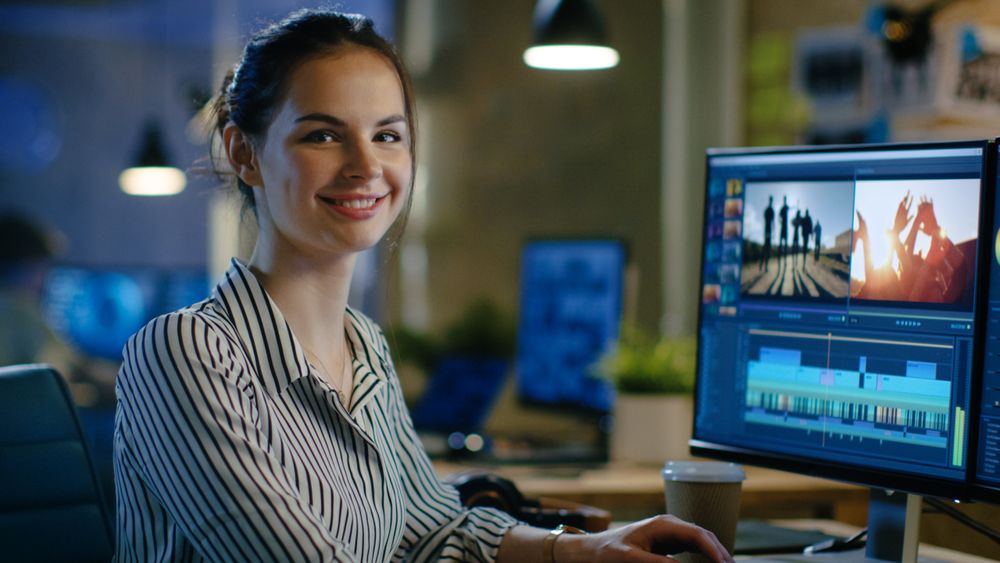 Female Video Editor Turns and Warmly Smiles into the Camera.