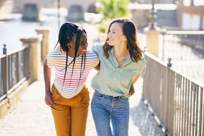 Female friends in casual clothing walking up cobble stone path with their arms around each other
