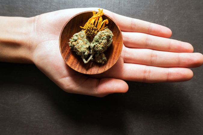 Hand holding a wooden container full of dried marijuana