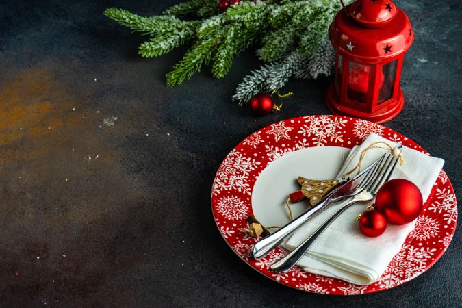 Holiday table setting on red plates with lantern and pine needles with copy space