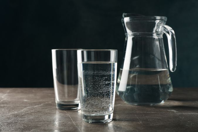 Two glasses of water in dark room on marble table with pitcher