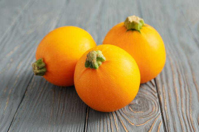 Three round zucchini on wooden background, close up