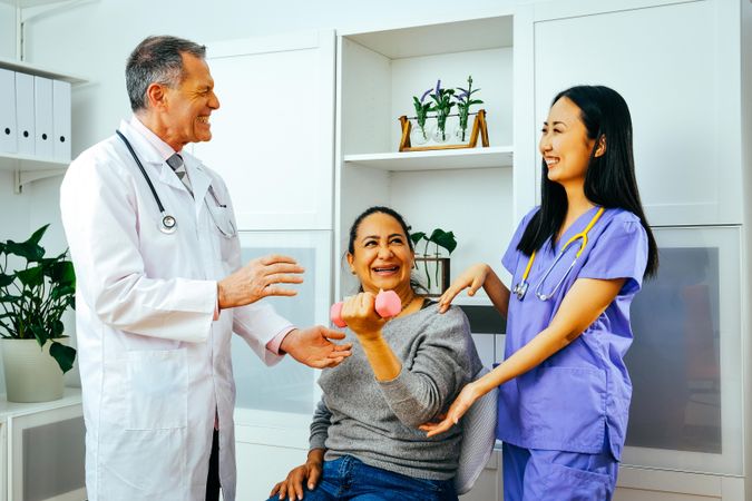 Doctor and physiotherapist helping patient with arm rehab exercises while sharing a joke