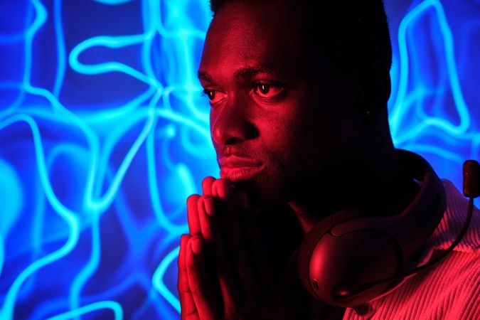 Thoughtful Black man with praying hands against neon light