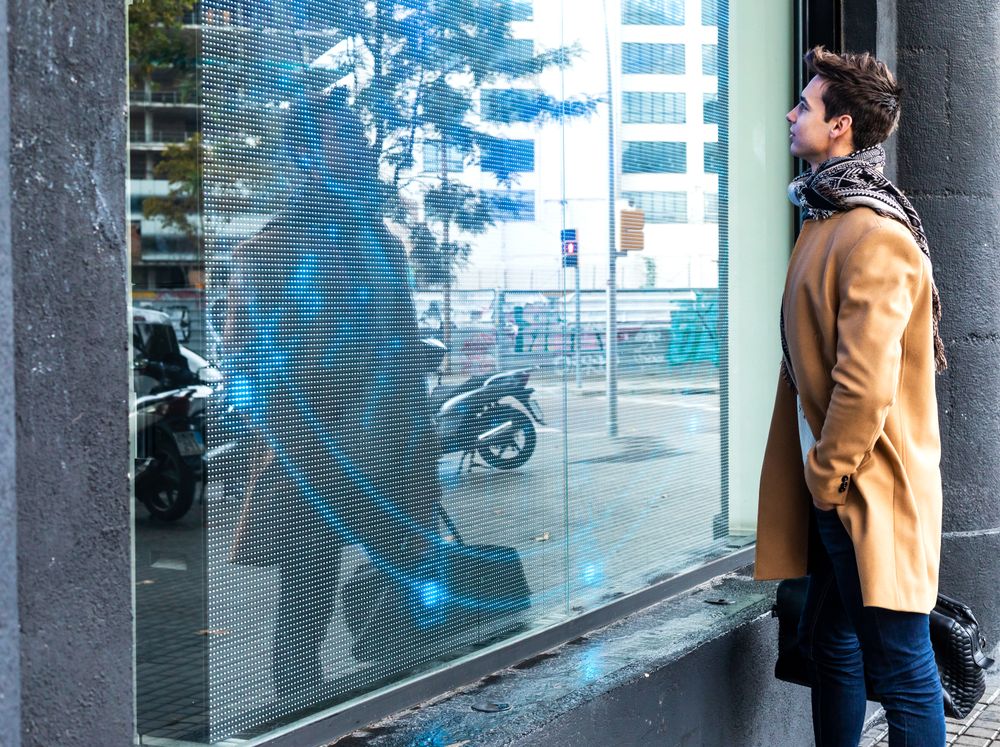 Man wearing camel coat and scarf looking through shop window