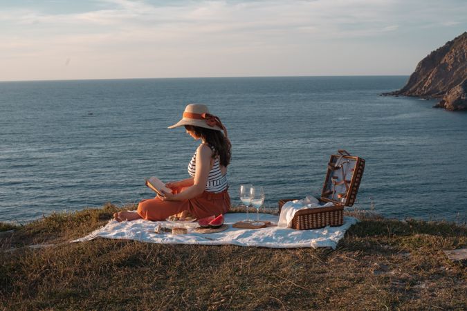 Woman reading on mat for picnic on seashore