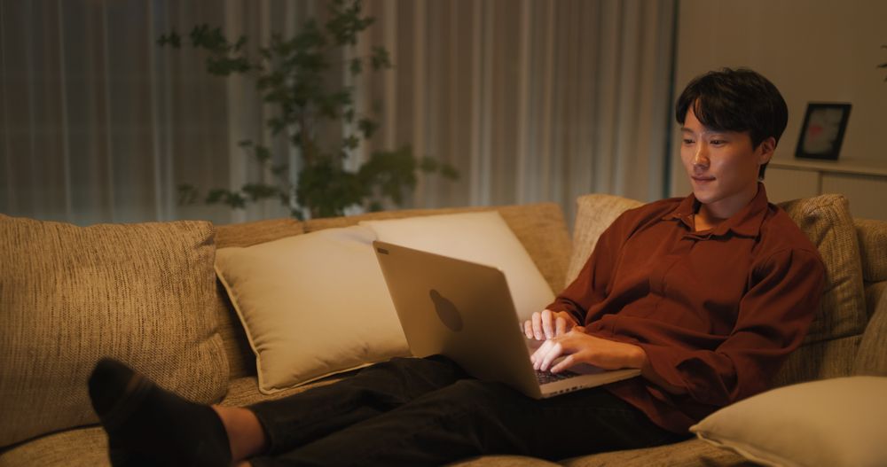 Young Asian Male Browsing Internet in The Evening in His Apartment, Using Laptop Computer at Home