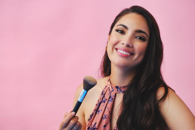 Head shot of smiling Hispanic woman looking at camera while holding large make up brush