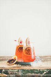 Two glasses of an orange cocktail on board, with blood orange slices, and cocktail picks, copy space