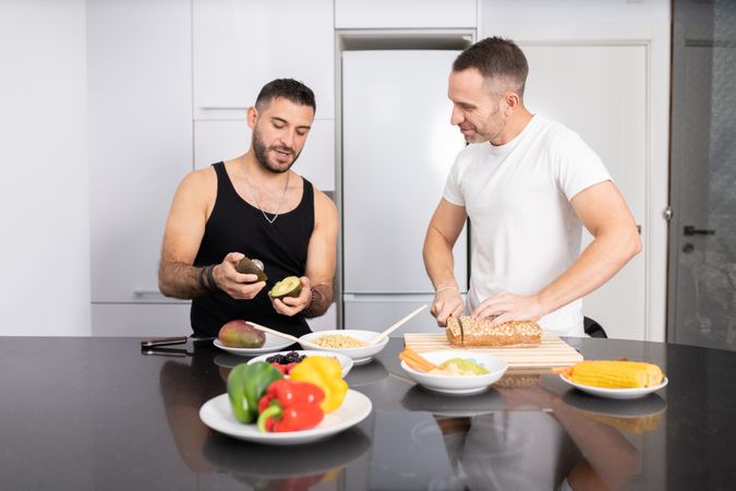 Happy male couple preparing vegetables and cutting bread for lunch