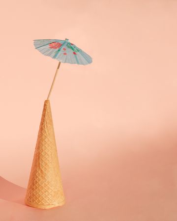 Ice cream cone with cocktail parasol on pink background