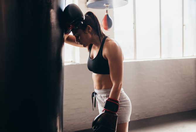 Female boxer resting her head on a punching bag
