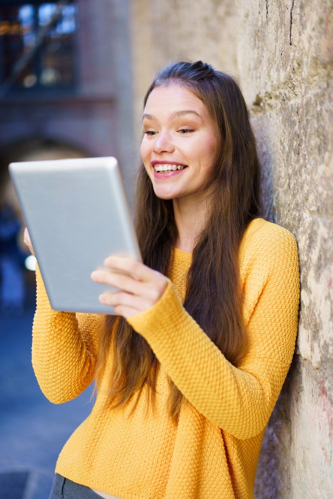 A Joyful Young Woman is Engaged with Her Tablet While in a Bustling Urban Setting