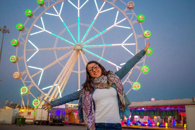 Smiling young woman near illuminated ferris wheel at night