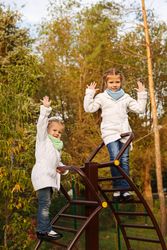 Two smiling young girls climbing playground stairs in park
