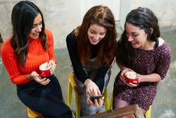 Women laughing at friends phone in coffee shop