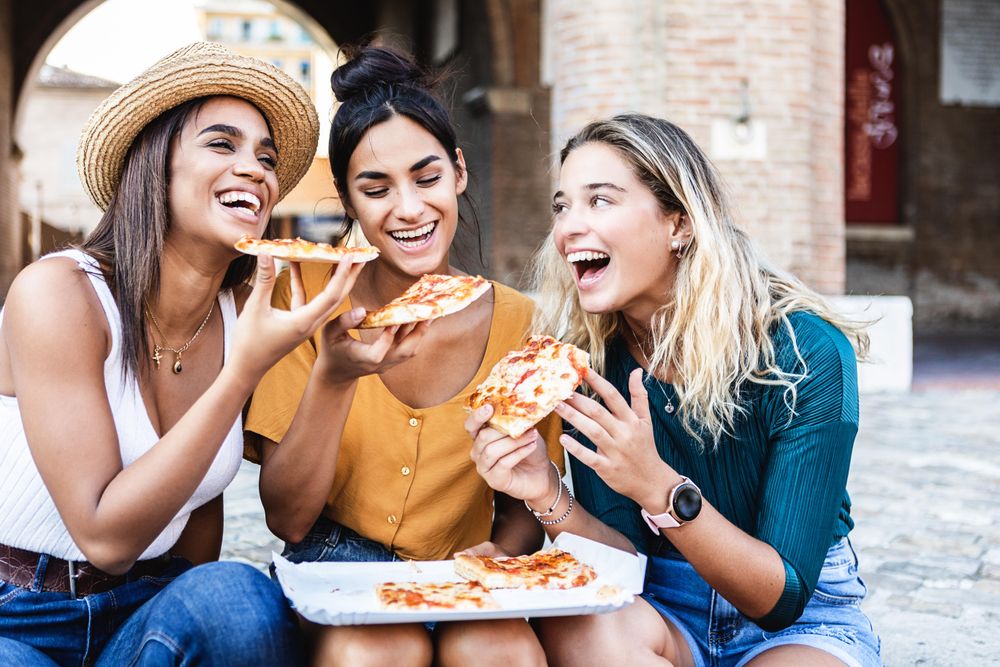 Three very happy female friends eating pizza on Italian street