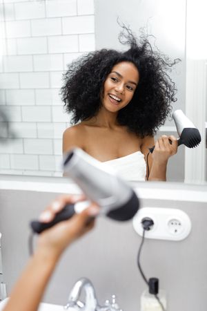 Playful woman styling her hair with blow dryer in bathroom