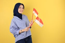 Cheerful Indonesian Muslim Woman in hijab celebrating Independence Day with Flag