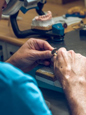 Unrecognizable dental technician polishing teeth at workplace