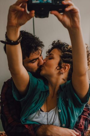 Joyful couple embracing and taking selfie on camera at home
