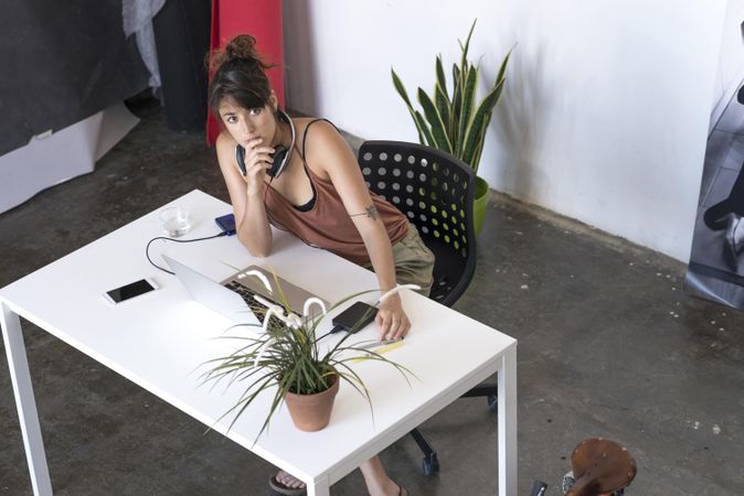 Woman thinking about something at desk with laptop and plant