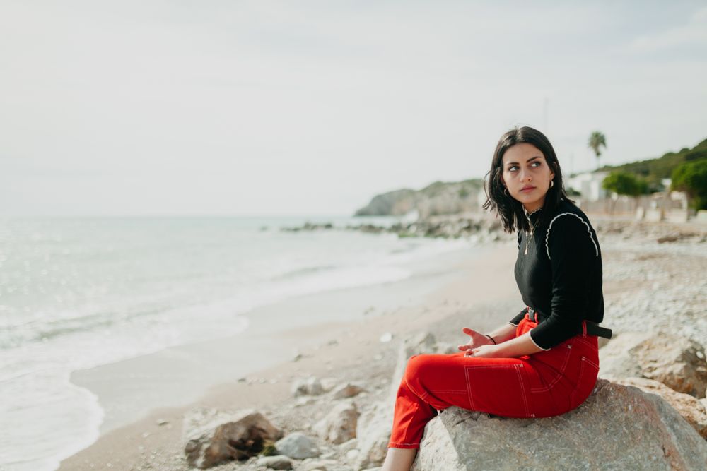 woman at sea leaning on stone looking away