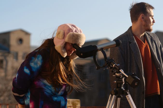 Girl in galaxy-pattern jacket adjusts solar telescope beside mentor